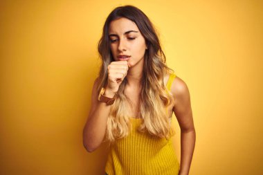 Genç güzel kadın sarı izole arka plan üzerinde t-shirt giyen rahatsız hissediyorum ve soğuk veya bronşit için bir belirti olarak öksürük. Sağlık kavramı.