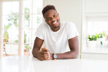 Evde beyaz masada Afro-Amerikan yakışıklı ile mutlu bir ve serin yüzündeki gülümseme. Şanslı kişi.