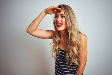 Çizgili t-shirt giyen genç güzel kadın beyaz izole arka plan üzerinde duran çok mutlu ve başının üzerinde el ile uzak görünümlü gülümsüyor. Arama konsepti.