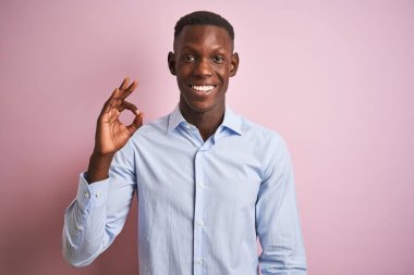 Izole pembe arka plan üzerinde duran mavi zarif gömlek giyen Afro-amerikan adam el ve parmakları ile ok işareti yapıyor olumlu gülümseyerek. Başarılı ifade.