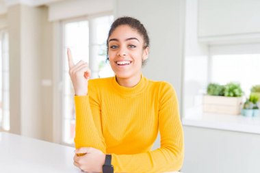 Yüzünde büyük bir gülümseme ile afro saçlı güzel genç afro-amerikan kadın, kameraya bakarak yan el ve parmak ile işaret.