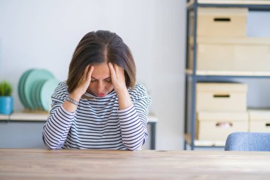 Orta yaş üst düzey kadın baş ağrısı umutsuz ve stresli evde masada oturan ağrı ve migren nedeniyle vurguladı. Eller baş.