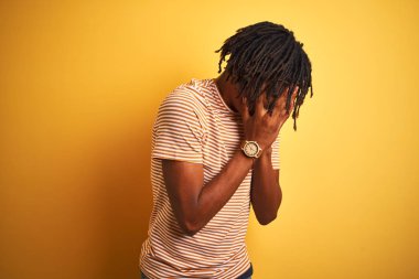 Dreadlocks çizgili t-shirt giyen Afro adam üzgün ifade elleri ile yüz kapsayan izole sarı arka plan üzerinde duran ağlarken. Depresyon kavramı.