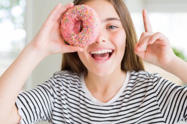 Güzel genç kız çocuk tatlı pembe donut yeme mutlu yüz, bir numaralı ile bir fikir ya da soru işaret parmağı ile şaşırttı