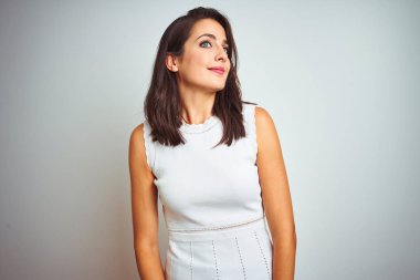 Beyaz izole arka plan üzerinde duran elbise giyen genç güzel kadın yan bakarak gülümseyerek ve düşünme uzak bakıyor.