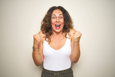 Orta yaş yaşlı kadın beyaz izole arka plan üzerinde ayakta sürpriz ve kollarını kaldırdı ve açık gözleri ile başarı için hayran kutluyor. Kazanan kavramı.