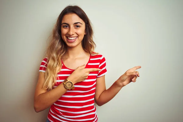 Young beautiful woman wearing red stripes t-shirt over white isolated background smiling and looking at the camera pointing with two hands and fingers to the side.