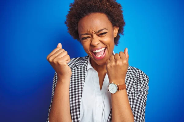 African american business executive woman over isolated blue background very happy and excited doing winner gesture with arms raised, smiling and screaming for success. Celebration concept.