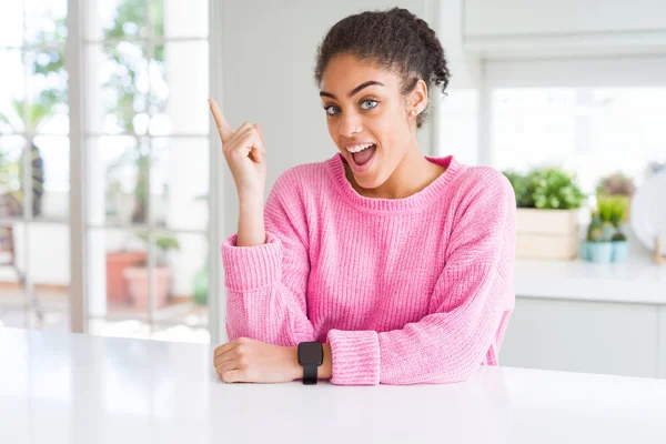 Beautiful african american woman with afro hair wearing casual pink sweater with a big smile on face, pointing with hand finger to the side looking at the camera.