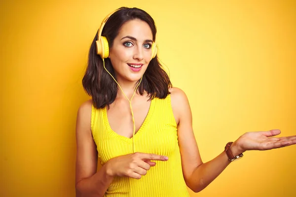 노란색 배경을 헤드폰을 사용하여 음악을 아름다운 여성은 놀라게하고 손으로 제시하고 — 스톡 사진