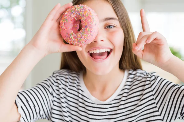 甘いピンクのドーナツを食べる美しい若い女の子の子供は幸せな顔で指を指すアイデアや質問で驚いた ナンバーワン — ストック写真