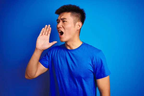 年轻的亚洲中国男子穿着T恤站在孤立的蓝色背景上 高喊着 用手捂住嘴大声地尖叫着 沟通概念 — 图库照片