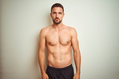 Izole arka plan üzerinde Genç yakışıklı gömleksiz adam yüzünde ciddi bir ifade ile rahat. Kameraya basit ve doğal bir bakış.