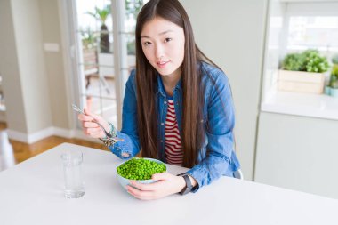 Güzel Asyalı kadın ciddi düşünme akıllı yüz üzerinde kendine güvenen bir ifade ile taze yeşil bezelye yeme