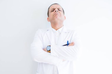 Orta yaş Doktor adam beyaz arka plan üzerinde tıbbi ceket giyiyor şüpheci ve sinir, kesişmiş kollar ile yüz üzerinde ifade onaylamıyor. Negatif kişi.