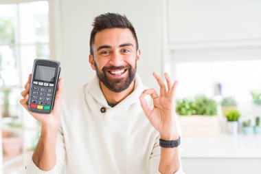 Yakışıklı İspanyol adam parmaklar, mükemmel sembolü ile ok işareti yapıyor satış terminal dataphone noktası tutan