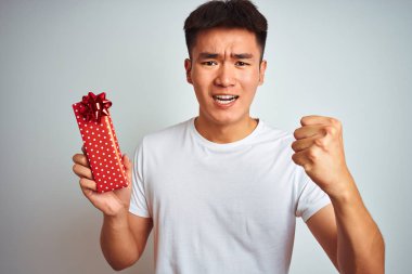 Genç asyalı Çinli adam izole beyaz arka plan üzerinde ayakta sevgililer mevcut tutan kızgın ve öfke ile bağırarak sinirli, deli ve yükseltilmiş el ile bağırıyor, öfke kavramı