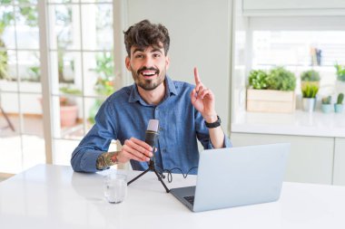 Genç adam kayıt podcast mikrofon ve dizüstü bilgisayar kullanarak mutlu yüz, bir numara ile bir fikir veya soru işaret parmağı ile şaşırttı