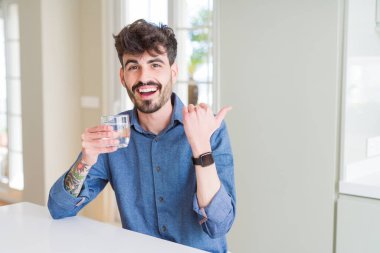 Taze bir bardak su içen genç adam işaret ederek ve mutlu yüzü gülümseyerek yan başparmağıile gösteren