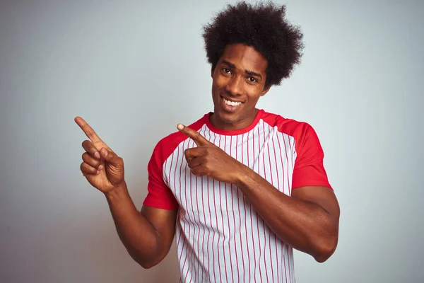 African american man with afro hair wearing red striped t-shirt over isolated white background smiling and looking at the camera pointing with two hands and fingers to the side.