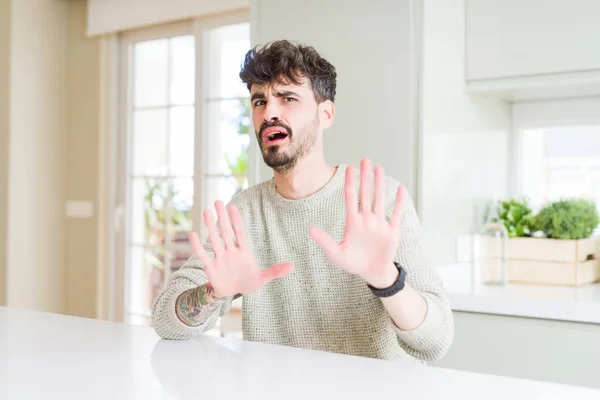 Joven Hombre Vistiendo Suéter Casual Sentado Mesa Blanca Asustado Aterrorizado — Foto de Stock