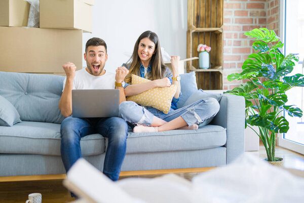 Young beautiful couple relaxing sitting on the sofa of new house using computer laptop screaming proud and celebrating victory and success very excited, cheering emotion