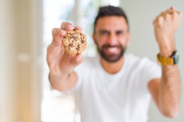 Yakışıklı İspanyol adam çikolata parçaları çerezleri yeme sinirli ve sinirli öfke ile bağırarak, deli ve yükseltilmiş el ile bağırıyor, öfke kavramı