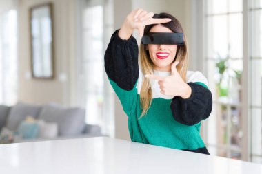 Genç güzel kadın gözleri siyah sansür bant ile evde mutlu yüz ile elleri ve parmakları ile çerçeve yapma gülümseyerek. Yaratıcılık ve fotoğrafçılık konsepti.