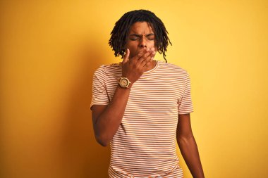 İzole sarı arka plan üzerinde duran çizgili t-shirt giyen dreadlocks ile Afro adam el ile ağız kapsayan yorgun esneme sıkılmış. Huzursuz ve uykululuk.