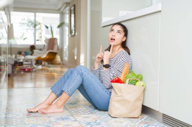 Genç kadın taze bakkal dolu bir kağıt torba ile mutfak katta oturan şaşırttı ve baktı ve parmakları ile işaret ve kolları kaldırdı şaşırttı.