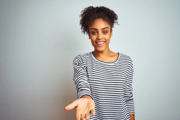 African american woman wearing navy striped t-shirt standing over isolated white background smiling cheerful offering palm hand giving assistance and acceptance.