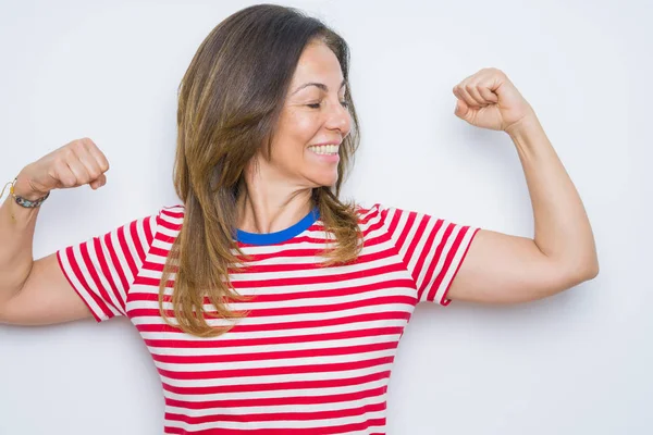 Orta yaş yaşlı kadın beyaz izole arka plan üzerinde duran kol kasları gururla gülümseyen gösteren. Fitness konsepti.