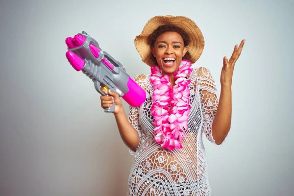 Young african american woman with afro hair wearing flower hawaiian lei and water gun very happy and excited, winner expression celebrating victory screaming with big smile and raised hands