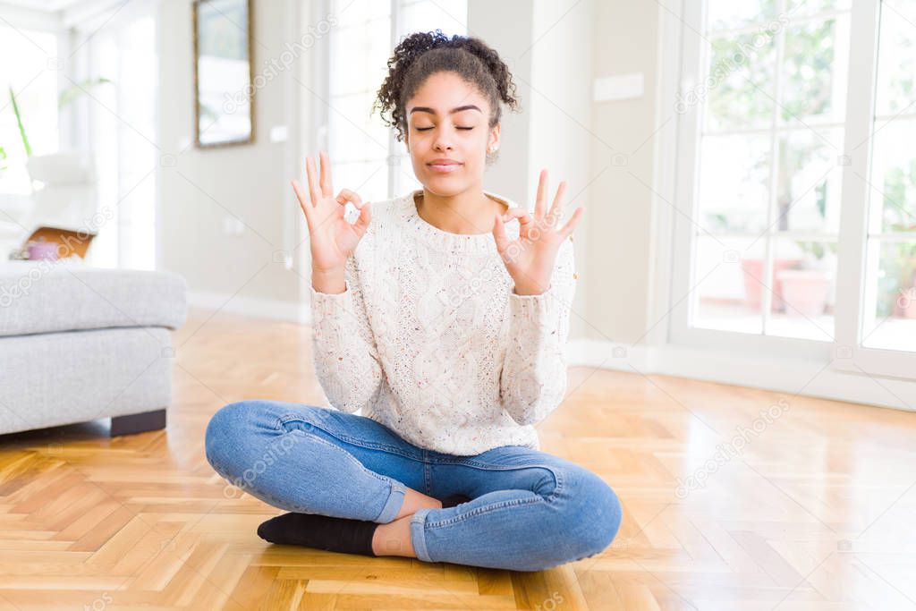 Beautiful young african american woman with afro hair sitting on the floor relax and smiling with eyes closed doing meditation gesture with fingers. Yoga concept.