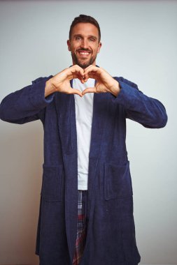 Rahat pijama ve cüppe giyen genç adam sabah izole arka plan üzerinde sevgi kalp sembolü ve elleriyle şekil gösteren gülümseyerek. Romantik kavram.