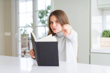 Güzel genç kız kamera ve size parmak ile işaret eden evde bir kitap okuma, el işareti, önden olumlu ve kendinden emin jest