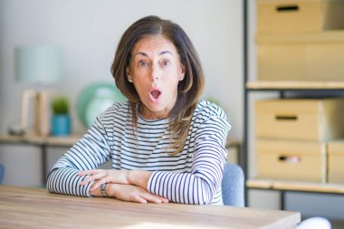 Orta yaş kıdemli kadın evde masa içinde oturan korkuyor ve sürpriz ifade, korku ve heyecanlı yüz ile şok.