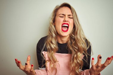 Genç çekici kadın beyaz izole arka plan deli ve deli bağırarak ve agresif ifade ve kollar kaldırdı ile bağırıyor üzerinde duran sweatshirt giyiyor. Hayal kırıklığı kavramı.