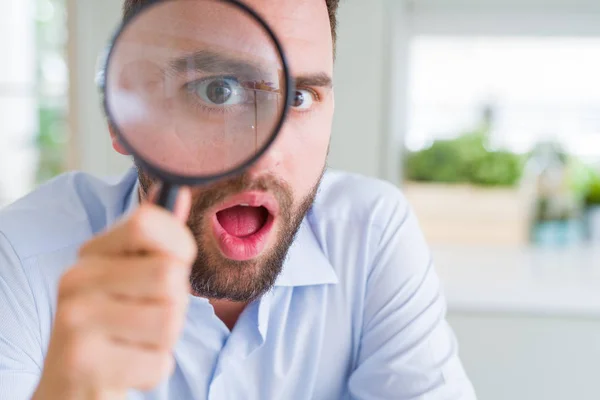 Handsome business man holding magnifying glass close to face, bi — Stock Photo, Image