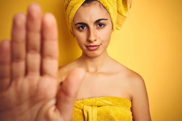 Young beautiful woman wearing a towel over yellow isolated background with open hand doing stop sign with serious and confident expression, defense gesture