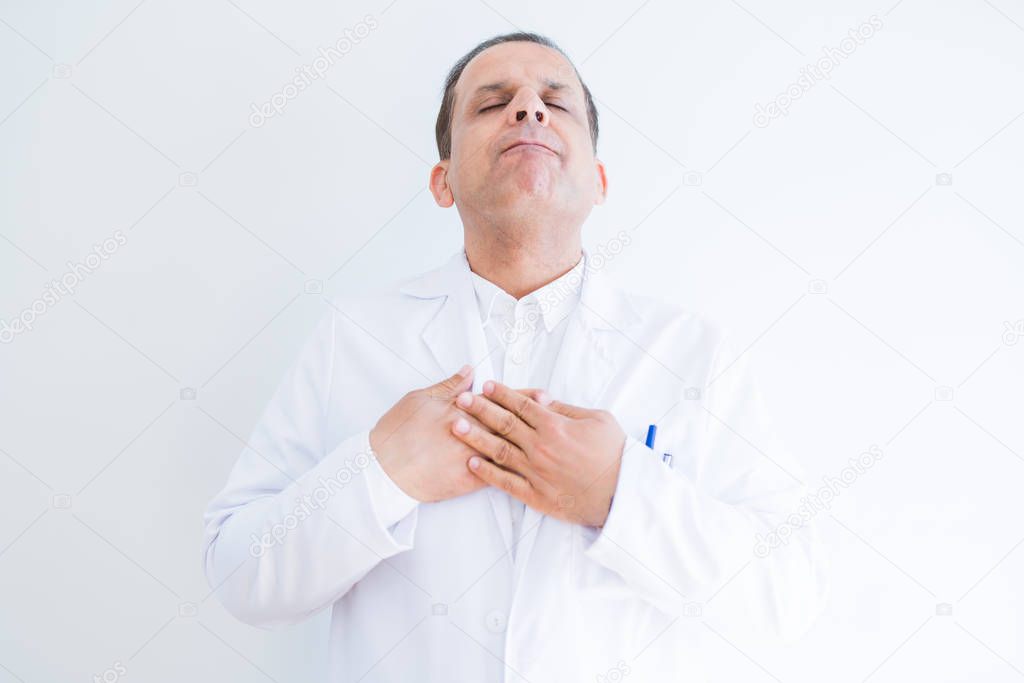 Middle age doctor man wearing medical coat over white background smiling with hands on chest with closed eyes and grateful gesture on face. Health concept.