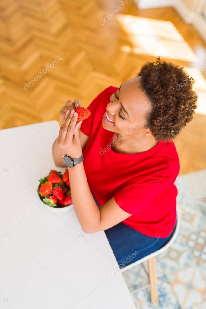 Beautiful young african american woman eating fresh red strawber