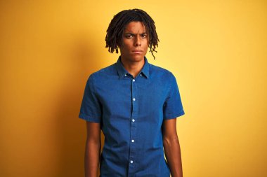 Yalnız sarı arka plan şüpheci ve sinir üzerinde duran rahat kot gömlek giyen dreadlocks ile Afro adam, sorun nedeniyle üzgün kaşlarını çatma. Negatif kişi.