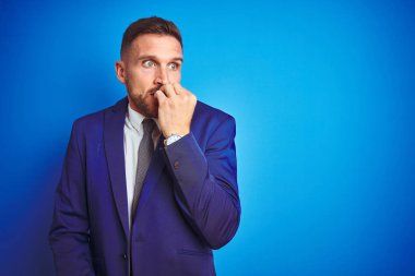 Mavi izole arka plan üzerinde genç yakışıklı iş adamı stresli ve ağız tırnak ısırma elleri ile sinir görünümlü. Anksiyete sorunu.