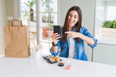 Akıllı telefon kullanarak uygulamadan gıda teslimatı sipariş eden güzel genç kadın el ve parmakla işaret etmekten çok mutlu