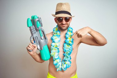 Yaz şapkası giyen genç adam ve Hawaii Lei çiçek kendini sürpriz yüz işaret parmak ile izole arka plan üzerinde su tabancası tutan