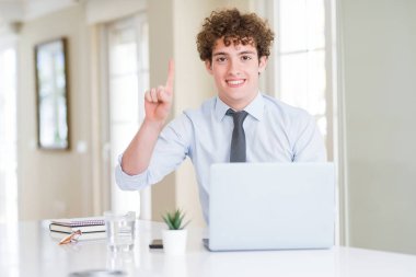 Ofiste bilgisayar dizüstü bilgisayar ile çalışan genç iş adamı gösteren ve kendinden emin ve mutlu gülümseyerek bir numaralı parmak ile işaret.