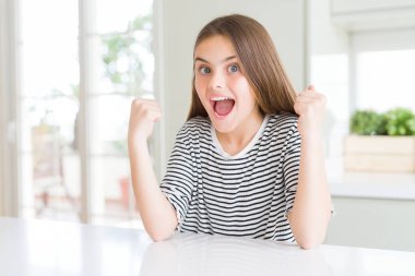 Güzel genç kız çocuk çizgili t-shirt giyen sürpriz ve kollarını kaldırdı ve açık gözleri ile başarı için şaşırttı kutluyor. Kazanan kavramı.