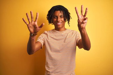Çizgili t-shirt giyen dreadlocks giyen Afro adam izole sarı arka plan üzerinde duran gösteren ve emin ve mutlu gülümserken parmakları sayısı sekiz işaret.