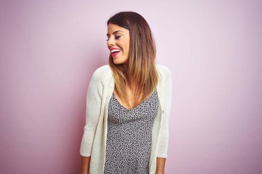 Genç güzel kadın pembe izole arka plan üzerinde duran yüzünde gülümseme, doğal ifade ile yan bakıyor. Gülmekten emin.